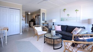 A living room with a sofa, two wicker chairs, a glass coffee table, and a ceiling fan.