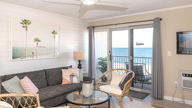 A living room with a gray sofa, wicker chairs, a glass coffee table, and a ceiling fan.