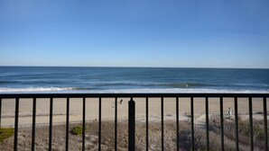 A beach view with a clear sky, a sandy shore, and a fence in the foreground.