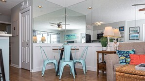 Eine moderne Küche mit Essbereich, ein Wohnzimmer mit Sofa und Couchtisch sowie ein Flur, der zu einer Tür mit der Aufschrift 'Basil' führt.