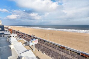 Une promenade en bois avec vue sur la plage, une enseigne indiquant « Wedgewood » et « Pizzeria », et un bâtiment doté d’un toit en pente.