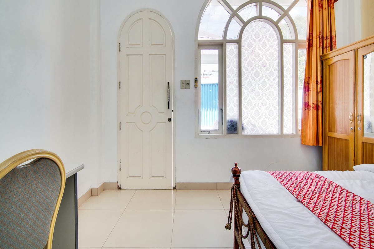Ein Zimmer mit einem Bett, einem Sessel, einer Tür und einem Vorhangfenster.