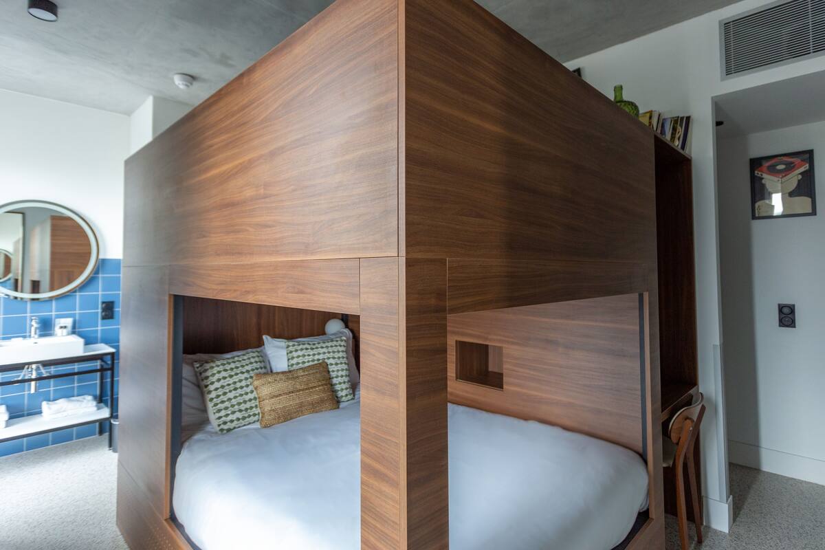 A modern room with a wooden bunk bed, a round mirror, a blue tiled wall, and a white sink.