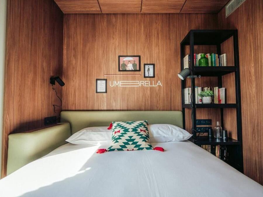 A hotel room with a bed, a bookshelf, and a wall-mounted sign.