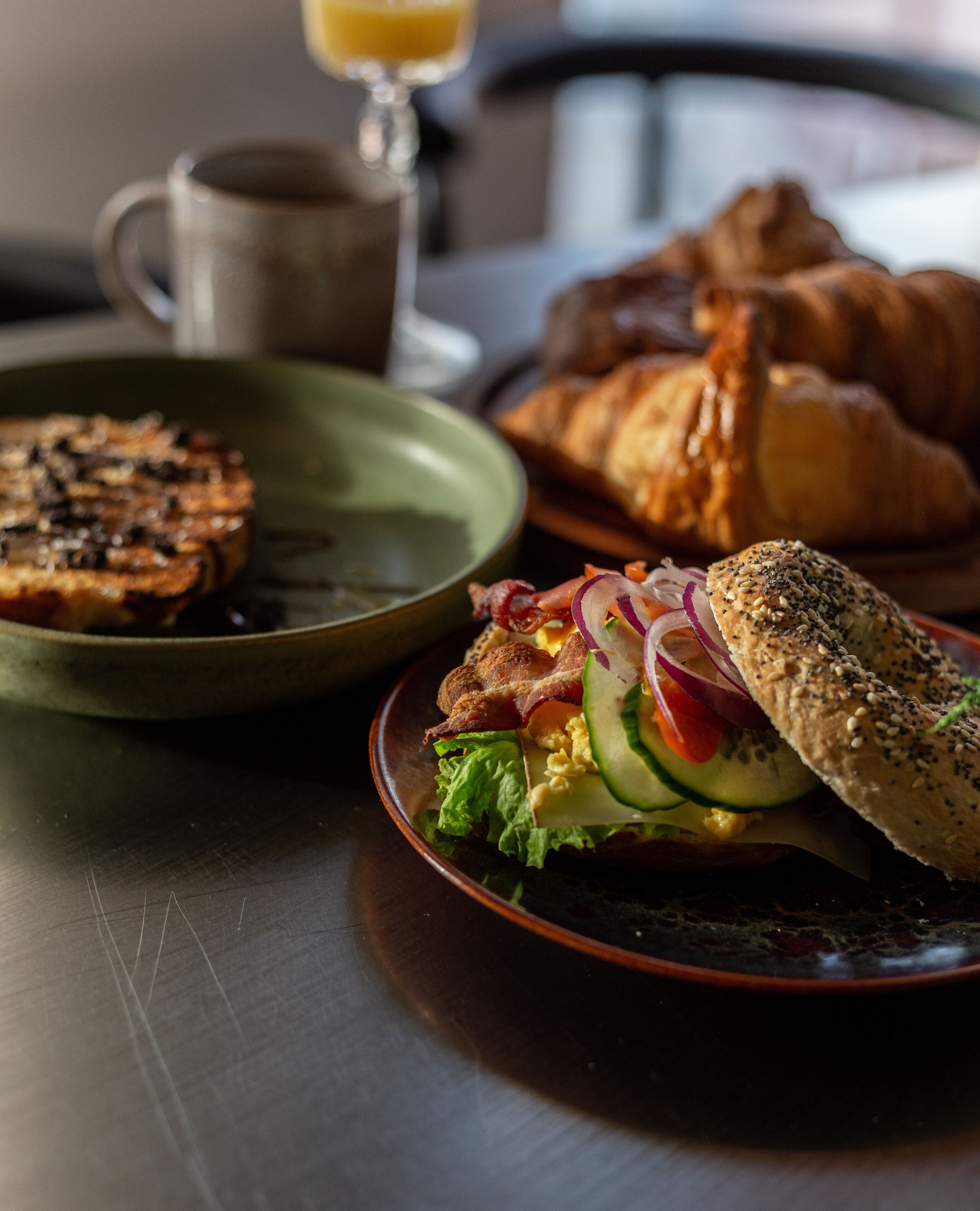 A breakfast setting with a croissant, a grilled sandwich, and a bowl of salad on a table.