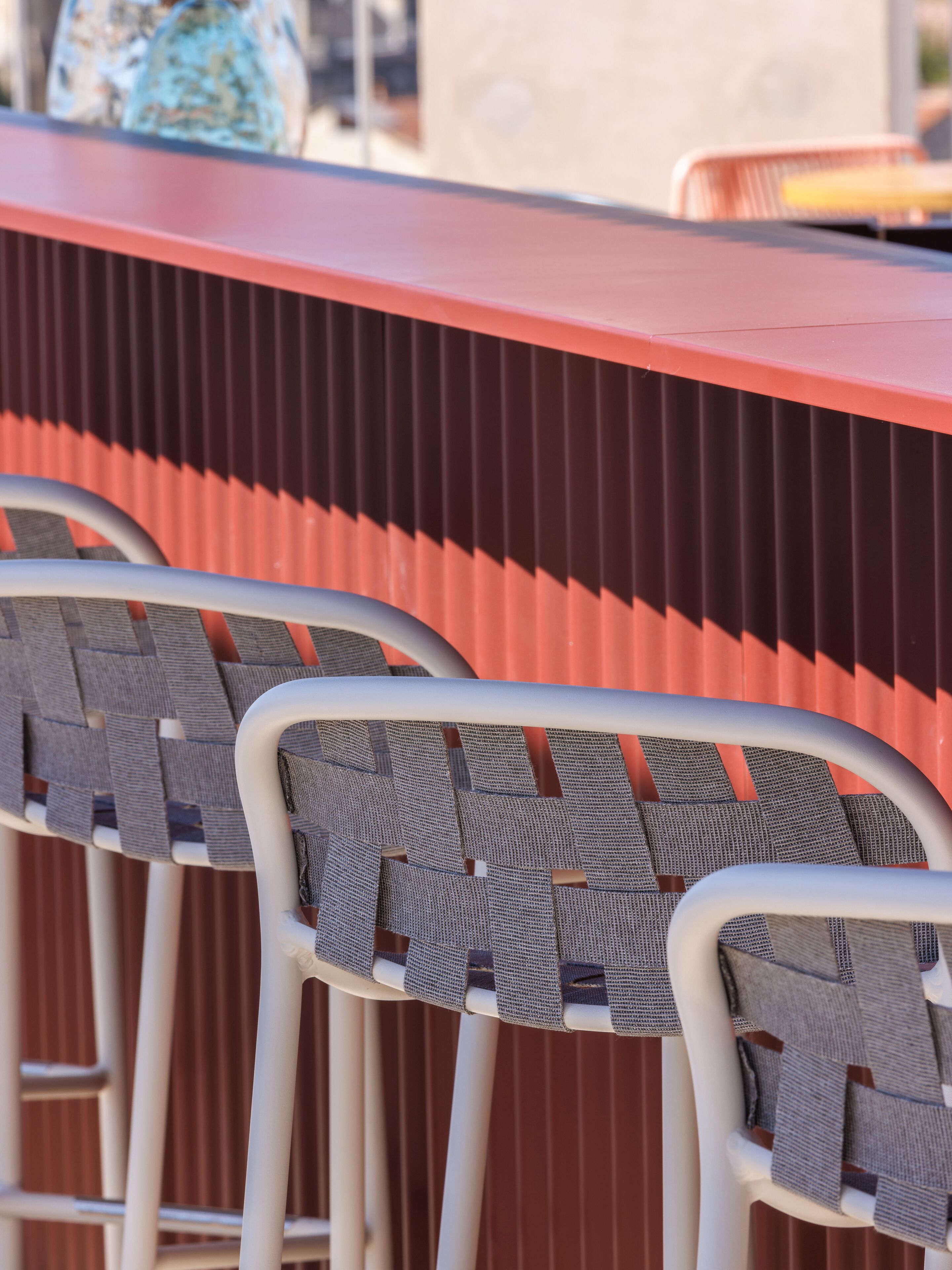 Uma área de bar com cadeiras de metal e um balcão vermelho.