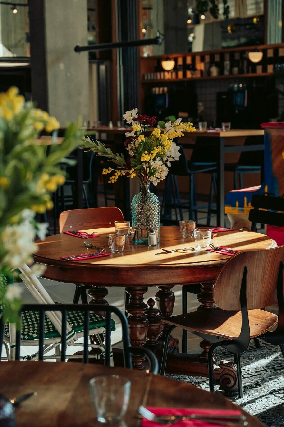 A dining table set with a vase of flowers, glasses, and cutlery.