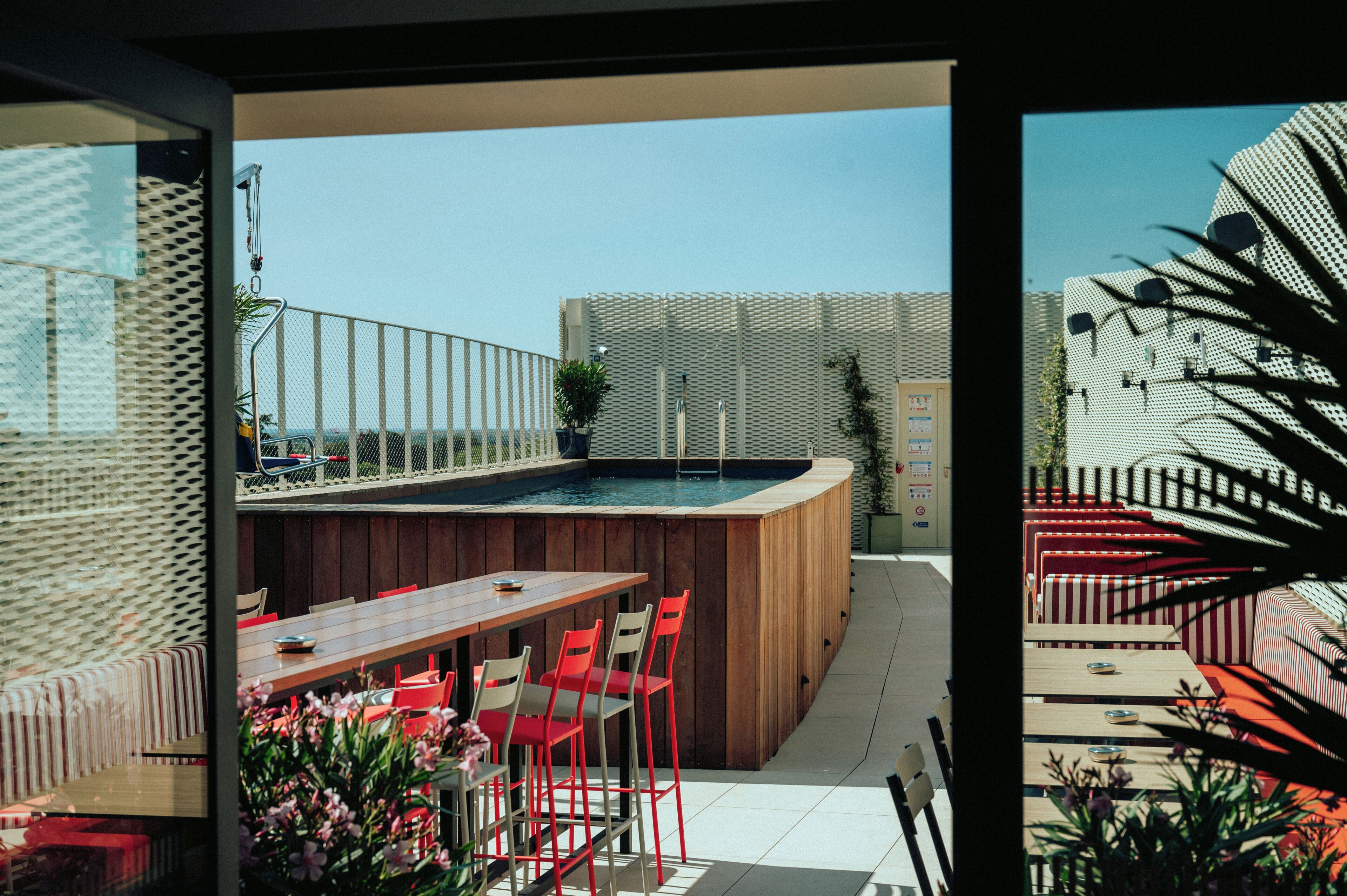 A poolside area with a wooden bar, red chairs, and a view of the pool.