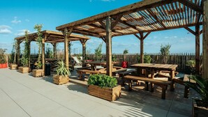 Un patio al aire libre con pérgolas de madera, mesas de picnic y jardineras con follaje.