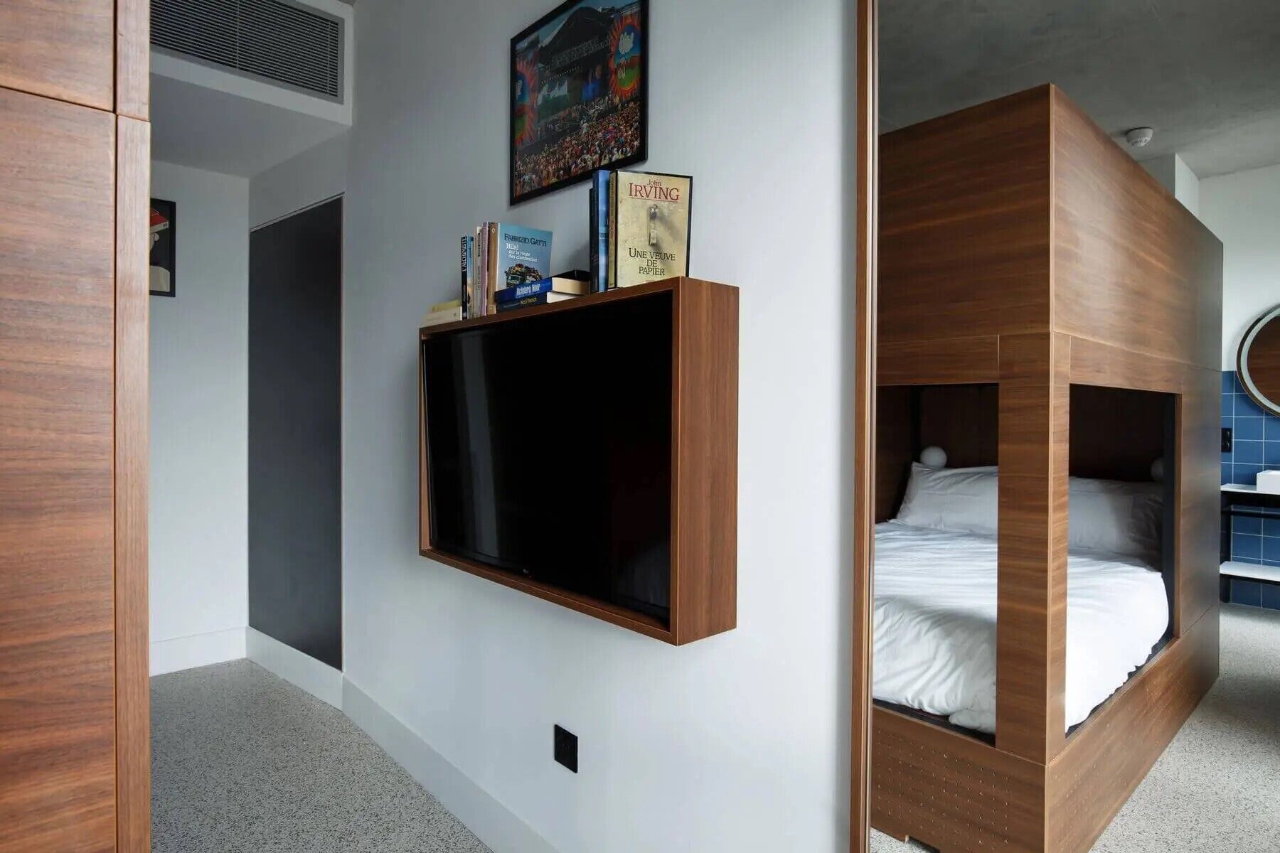 A modern bedroom with a built-in TV, a bookshelf, and a bunk bed.
