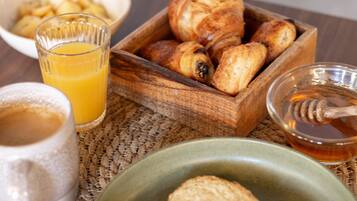 Desayuno con cruasanes, pan, jugo y miel sobre un posavasos tejido.