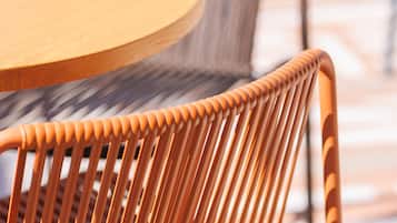 A close-up of a round wooden table and a wicker chair with a metal frame.