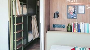 Une chambre avec un lit superposé, une table de chevet avec une lampe, une étagère murale avec des livres et un tableau encadré.
