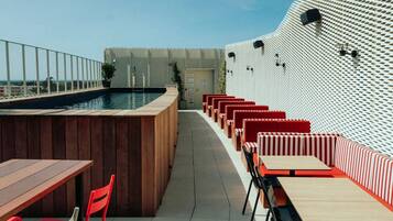 A rooftop pool area with wooden seating and a patterned wall.