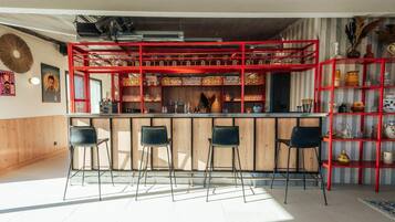 A bar area with a red metal structure, wooden counter, and black bar stools.