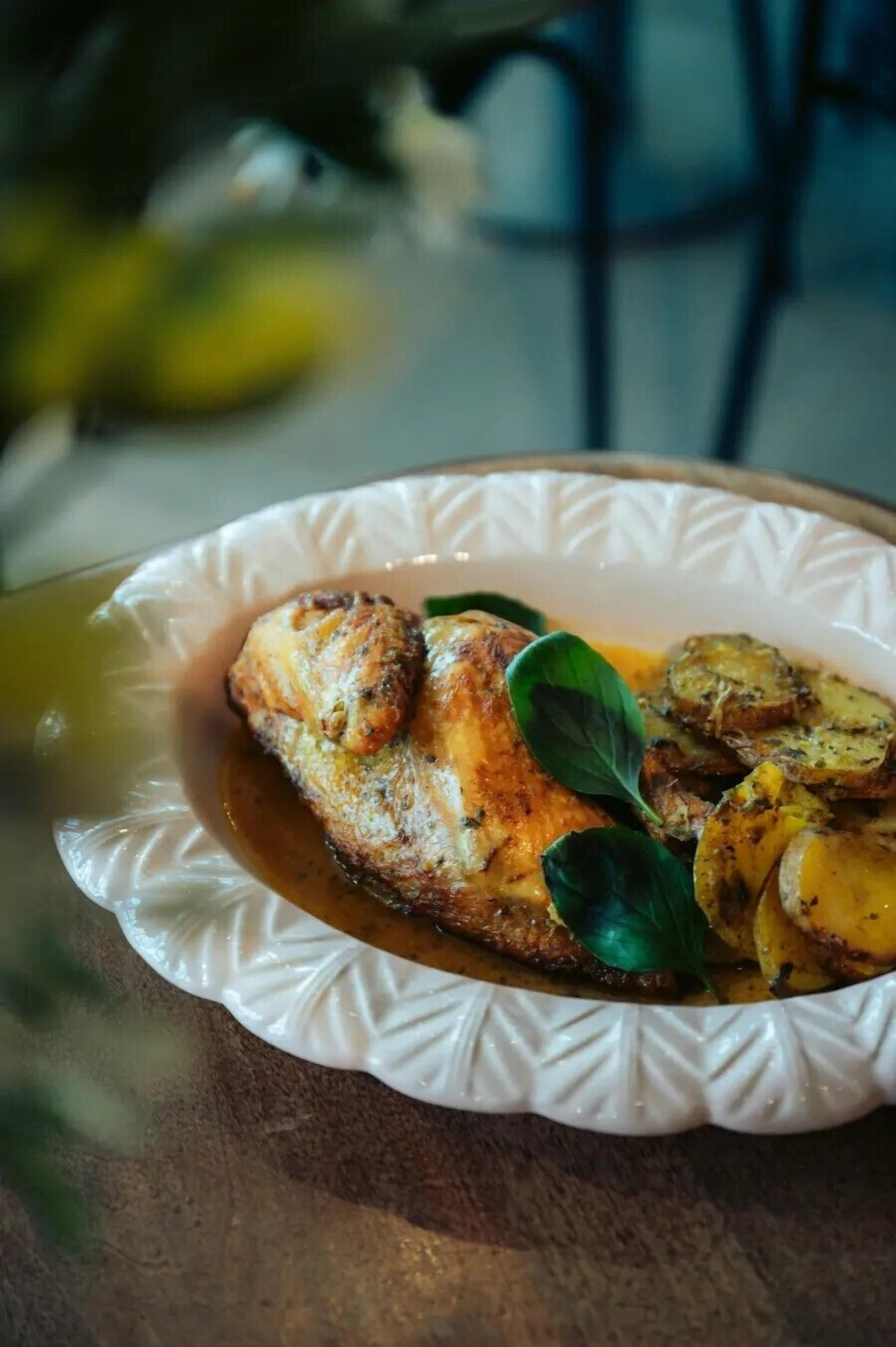 A plate of food with a fish, potatoes, and a basil leaf.