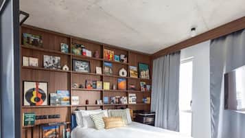 Un dormitorio con una cama grande, una estantería de madera llena de libros y adornos, un televisor en la pared y una ventana con cortinas.
