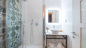 Un baño moderno con cabina de ducha de vidrio, un lavamanos blanco y un espejo encima.
