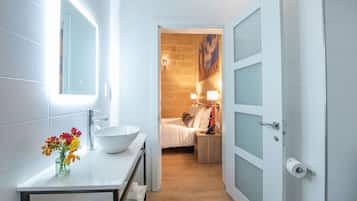 A modern bathroom with a white sink, mirror, and a vase of flowers.