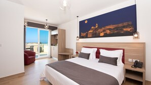 A modern hotel room with a large bed, a red sofa, a balcony with a view, and a painting of a cityscape. - Georges Boutique Living (Xaghra)