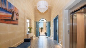 A hallway with a bench, a chandelier, and an elevator. - Georges Boutique Living (Xaghra)