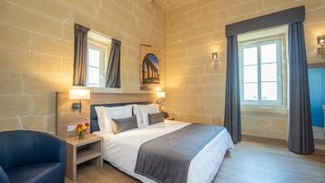 A hotel room with a large bed, a nightstand with a lamp, a chair, and a window with curtains.