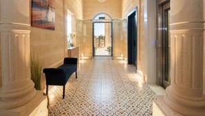 A hallway with a patterned floor, a bench, a painting, and an elevator. - Georges Boutique Living (Xaghra)