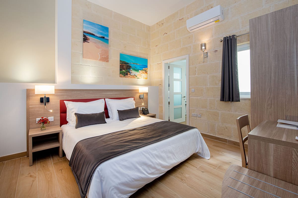 Una habitación de hotel moderna con una cama grande, cabecero de madera, mesitas de noche con lámparas, un escritorio y una silla.