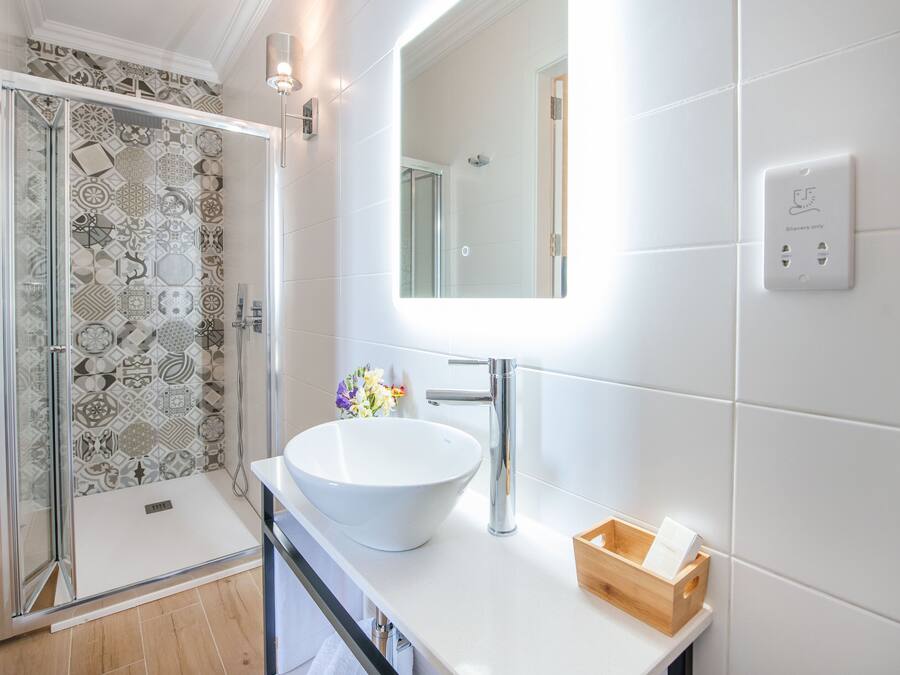 A modern bathroom with a large white sink, a glass shower enclosure, and a patterned tile wall.