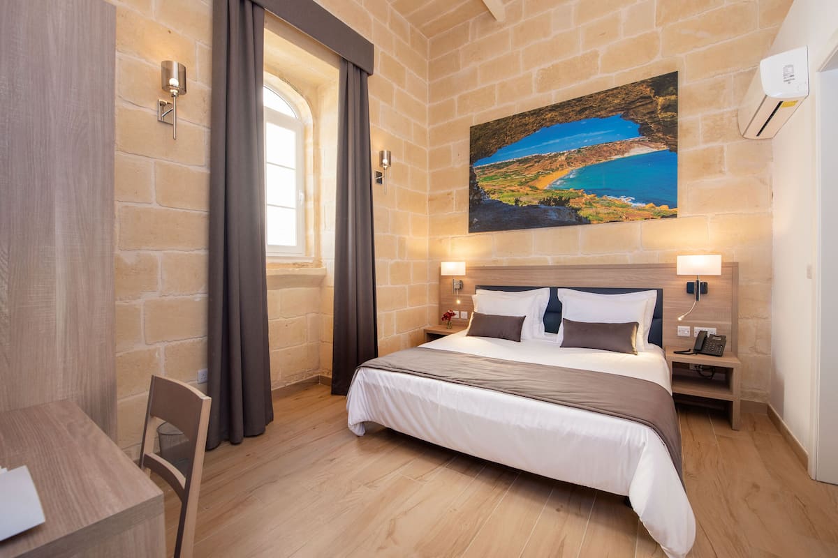 Habitación de hotel con una cama grande, un escritorio, una silla, un cuadro en la pared y una ventana con cortinas.