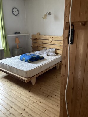 Un lit en bois avec un matelas, des oreillers et une couverture bleue. On peut voir une horloge murale et une petite table avec une lampe.