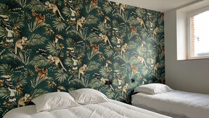 Una habitación con dos camas, un ventanal grande e impresión de animales tropicales en una pared.