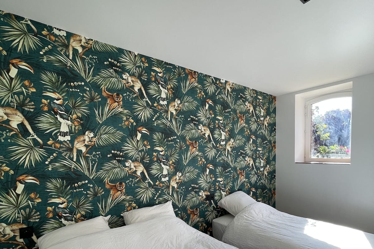A bedroom with two beds, a window, and a wall with a tropical animal print.