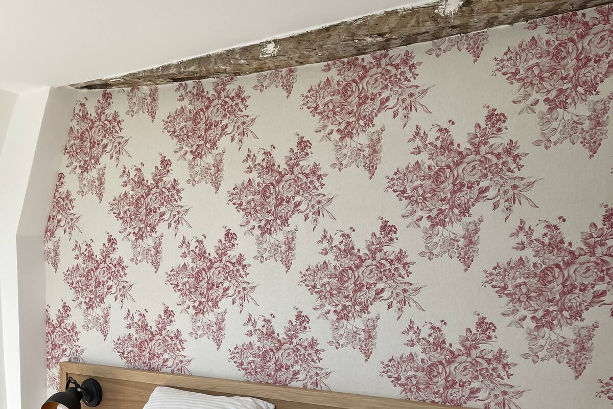 A bedroom with a wooden headboard, floral wallpaper, two bedside lamps, and a neatly made bed.