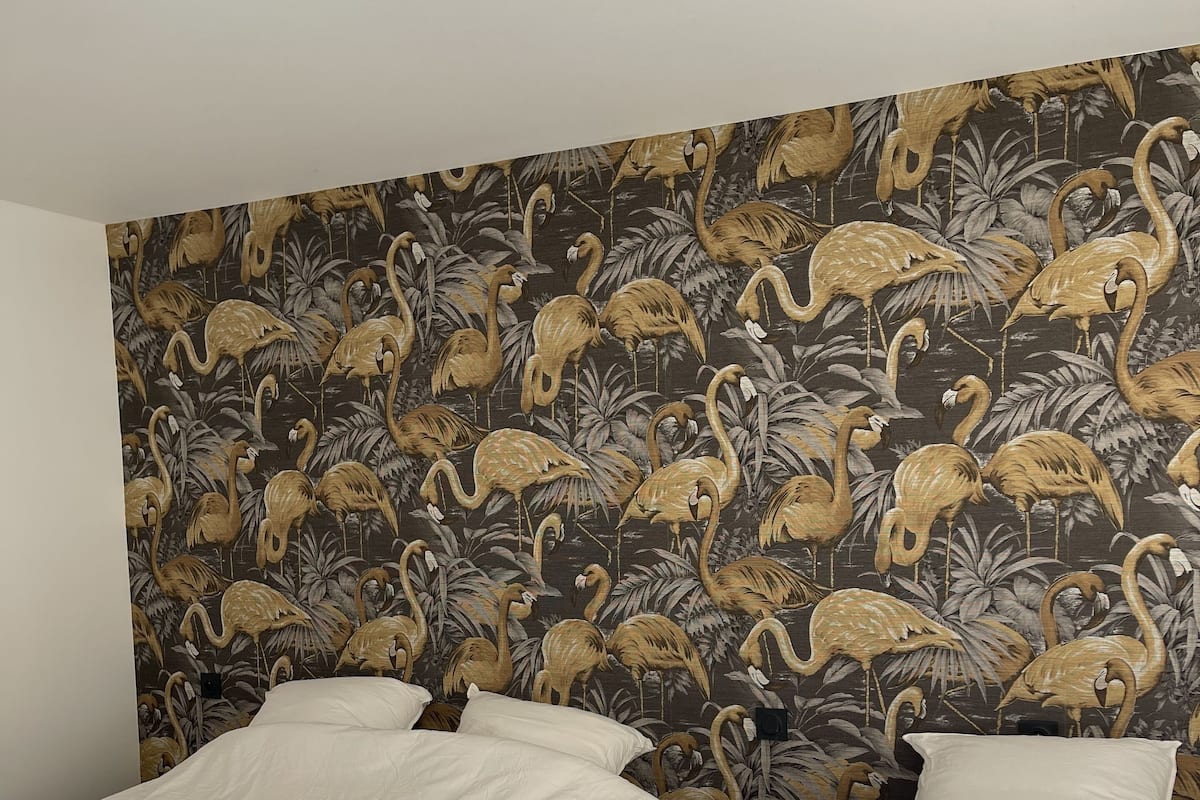A hotel room with two beds, a dark floral wallpaper, and a ceiling light fixture.