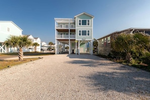 A two-story building with a balcony, a gravel driveway, and palm trees.
