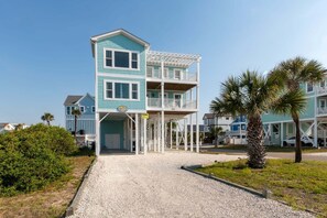 Ein zweistöckiges Strandhaus mit überdachter Veranda und Auffahrt mit Kies.