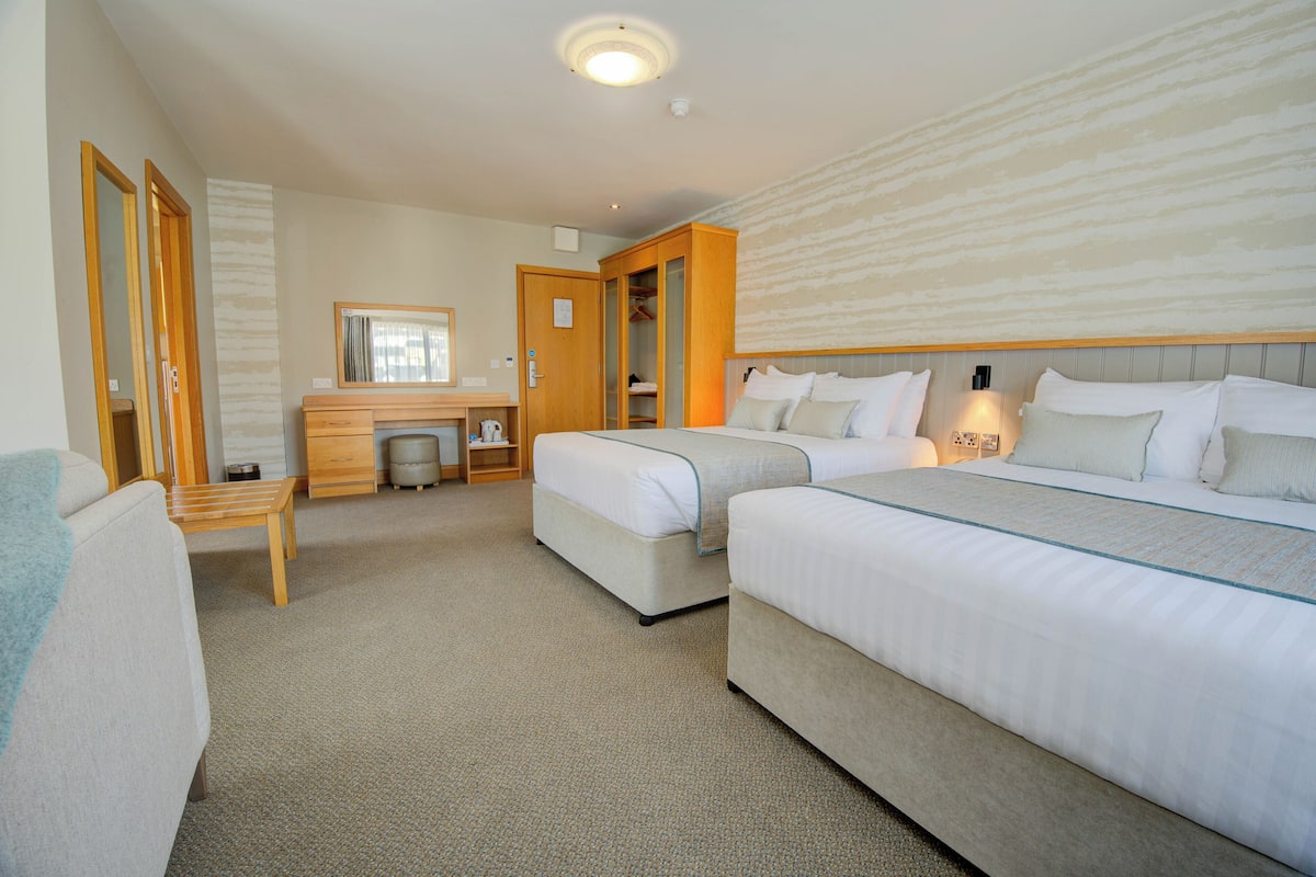 A hotel room with two beds, a desk, a mirror, and a wardrobe.