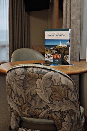 Een stoel met een bloemmotief, een tafel met een brochure met de titel 'Welcome to County Donegal', en een raam met gordijnen.
