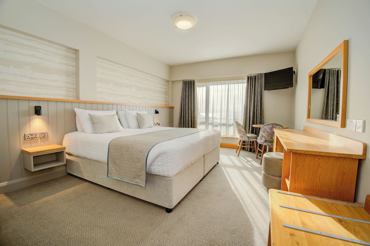 A hotel room with a bed, bedside table, chair, desk, and a TV mounted on the wall.