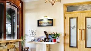 A reception area with a stone wall, a wooden reception desk, a framed picture, and a sign for Beach Hotel Downings. - Beach Hotel (Downings)