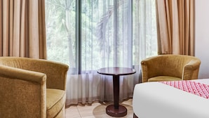 A hotel room with two armchairs, a small round table, and a bed with a red and white patterned bedspread. - Collection O 91071 Hotel Desa Wisata Tmii (Jakarta)