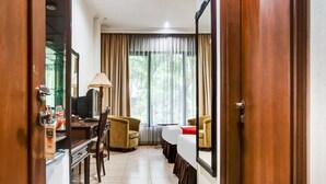 A hotel room with a wooden floor, a desk with a lamp, a chair, a bed with a red blanket, and a large mirror. - Collection O 91071 Hotel Desa Wisata Tmii (Jakarta)