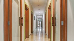 A long, well-lit hallway with wooden doors and green accents, leading to a bright room with a glass door. - Collection O 91071 Hotel Desa Wisata Tmii (Jakarta)