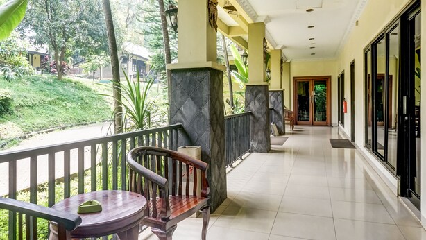 A corridor with a bench and table, a view of greenery outside, and a door leading to another room. - Collection O 91071 Hotel Desa Wisata Tmii (Jakarta)