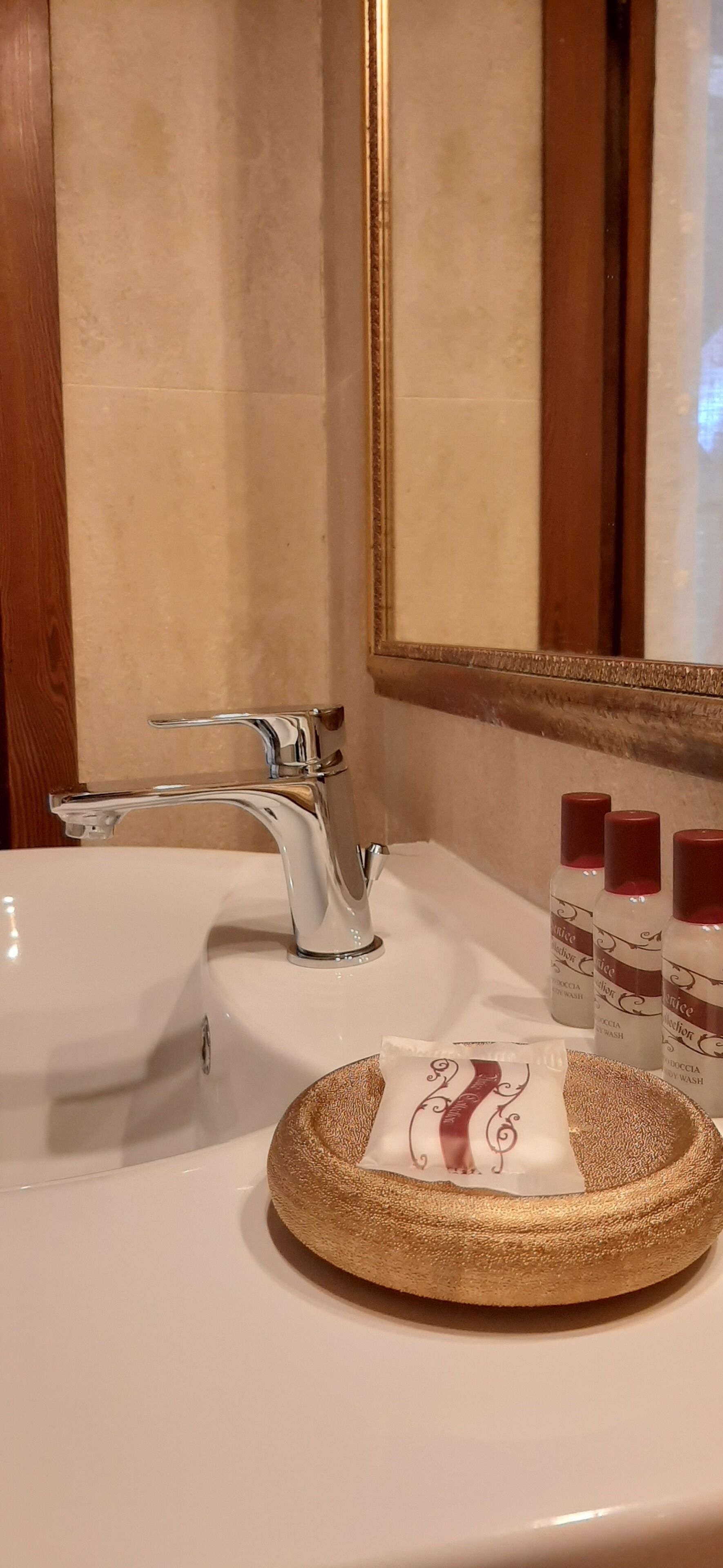 A bathroom sink with a modern faucet, a round gold soap dish, and three bottles of soap.