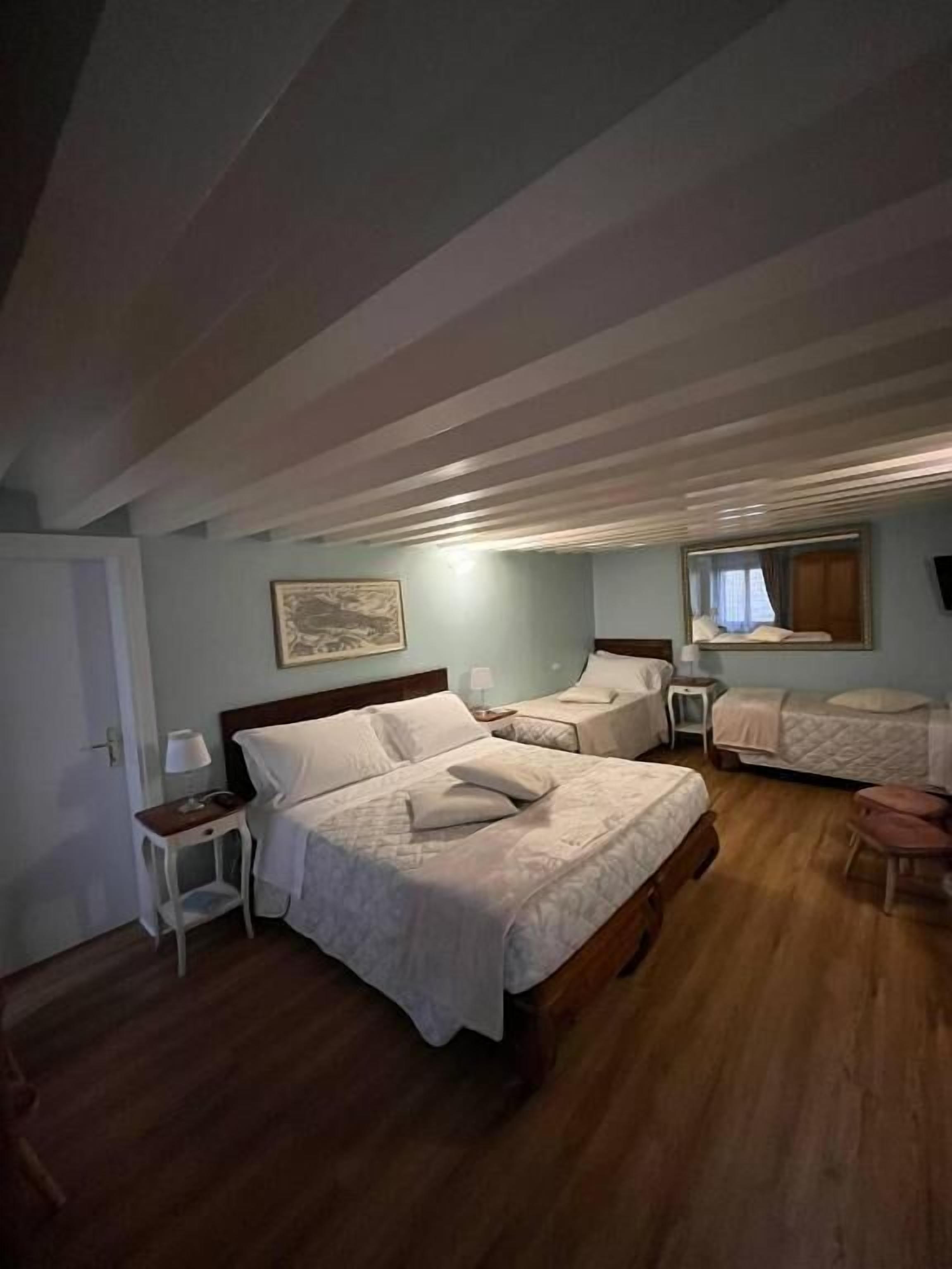 A bedroom with two beds, a wooden floor, a small table with a lamp, and a framed picture on the wall.