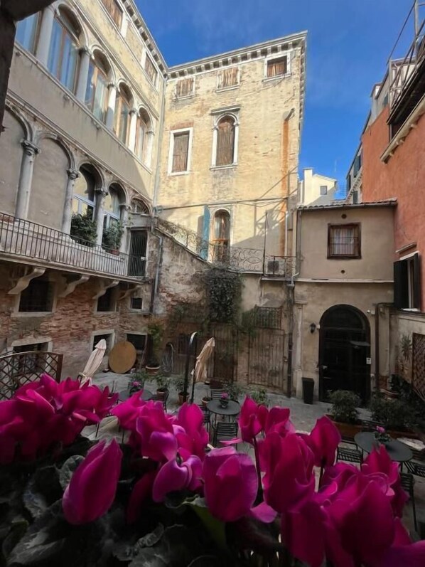 A courtyard with a building featuring arched windows and a balcony, surrounded by other structures.