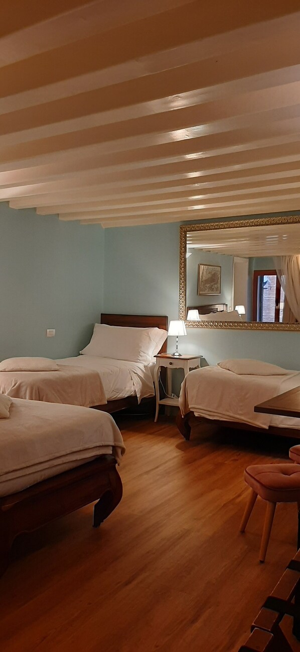 A hotel room with two single beds, a wooden floor, a desk with a lamp, and a large mirror.