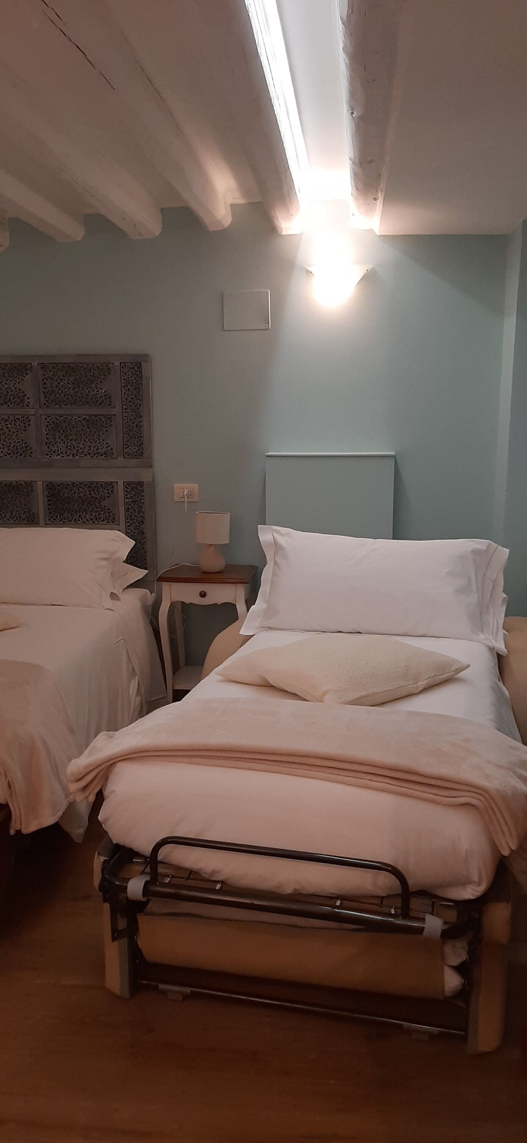 Una habitación de hospital con dos camas, una mesita de noche con una lámpara y una ventana con vistas.